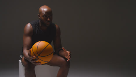 Studioaufnahme-Eines-Sitzenden-Männlichen-Basketballspielers-Mit-Händen,-Die-Den-Ball-Halten
